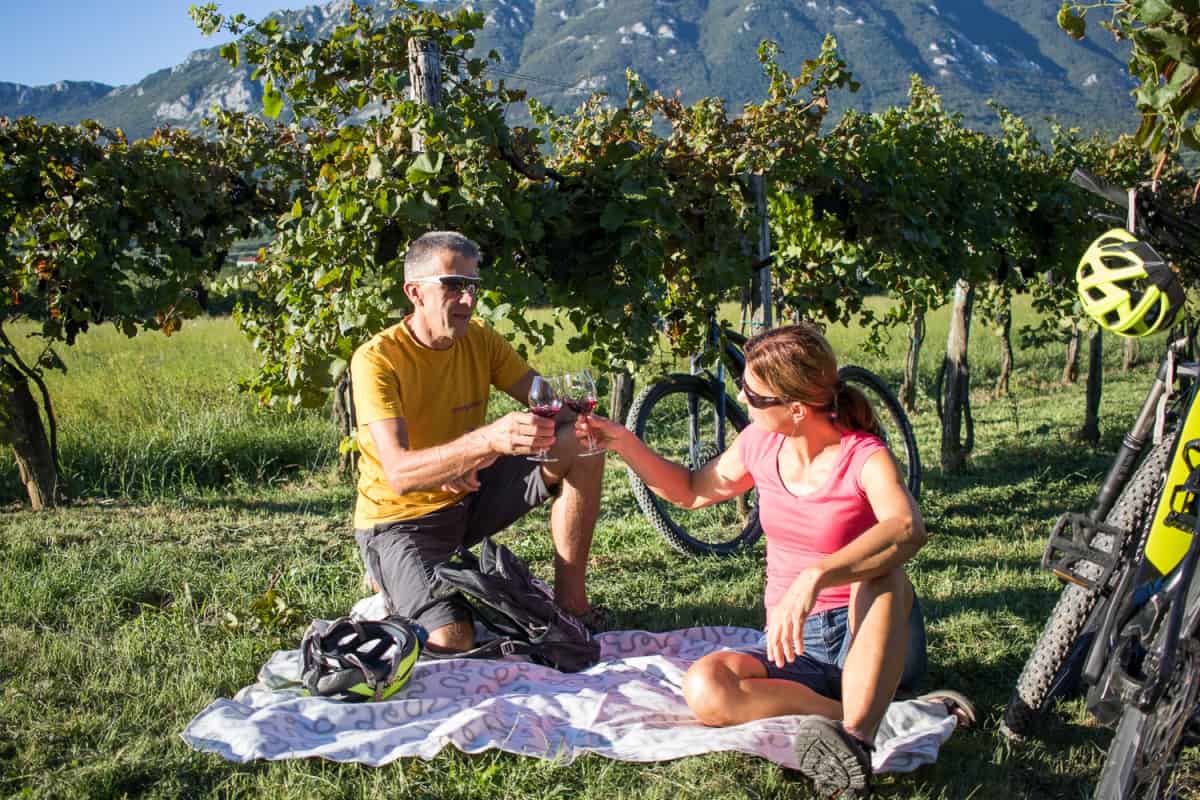 A couple enjoying wine in the middle of vineyards. Pick-nic style. E-bike tour of Vipava Valey by RockVelo.